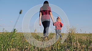 A young mother walks with her blonde daughter in the fresh air. Happy family walking on green grass.