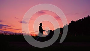 A young mother walks with a stroller near the rapeseed field at sunset.