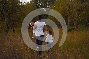 A young mother walks on yellow grass with her children after sunset