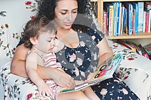 A young mother will her little toddler son sat on her lap as she reads a picture storybook