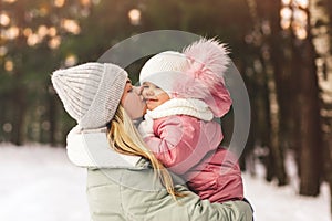 Young mother in winter holds her little daughter in her arms and kisses her. Family portrait. Motherhood and childhood