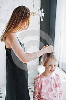 Young mother woman with long hair in black dress and little tween girl daughter in pajamas having fun in the morning at home,