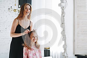 Young mother woman with long hair in black dress and little tween girl daughter in pajamas having fun in the morning at home,