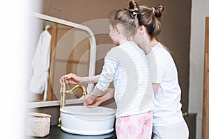 Young mother woman with long hair with little tween girl daughter in pajamas washing face and hands in the morning at home, family