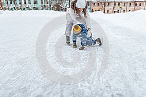 Young mother woman raises son boy 2-3 years ice in winter in city park. The concept of first lesson on skating support