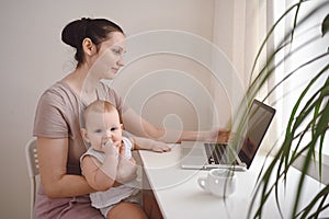 Young mother work studying from home with laptop computer during quarantine, little cute toddler baby on lap. Home office,