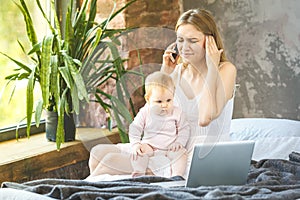 Young mother working from home, talking on smartphone while spending time with her baby girl. Freelance. Working home.