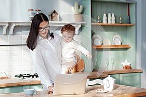 Young mother works at home with a laptop with a baby in her arms, remote work on maternity leave