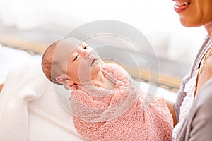 Young mother wrapping her little baby girl with pink blanket.