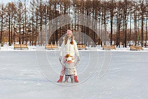 Young mother and young daughter stand in full growth in winter on ice