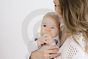 Young mother and a young son. A mother holds her baby in her arms. The baby keeps his hands in his mouth. Happy motherhood and chi