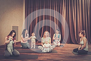 Young mothers and their babies doing yoga exercises on rugs at fitness studio.