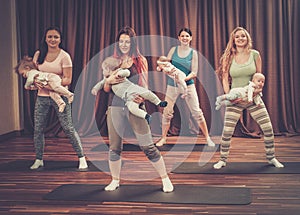 Young mothers and their babies doing yoga exercises on rugs at fitness studio.