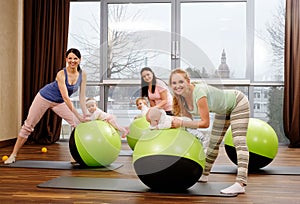 Young mothers and their babies doing yoga exercises on rugs at fitness studio.