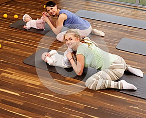 Young mothers and their babies doing yoga exercises on rugs at fitness studio.