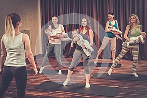 Young mothers and their babies doing yoga exercises on rugs at fitness studio.