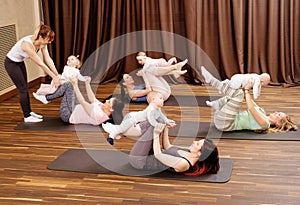 Young mothers and their babies doing yoga exercises on rugs at fitness studio.