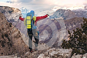 Young mountaineer standing with backpack on top of a mountain