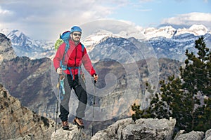 Young mountaineer standing with backpack on top of a mountain