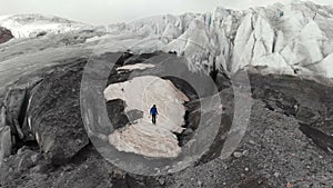 A young mountaineer in sunglasses in a cap and crampons stands on a large glacier with huge cracks in the mountains of