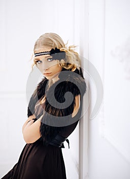 Young movie star of roaring twenties posing isolated on white background. Blond girl in headband with flower and fur