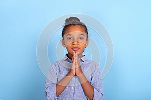 Young mulatta frizzy girl  prays against a blue background with copy space