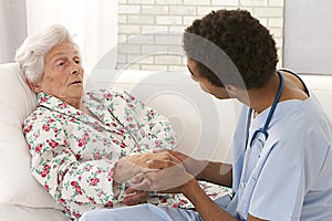 Young mulatto doctor caring about a very old female patient photo