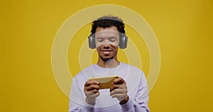 A young mulatto man in headphones plays on the mobile and smiling