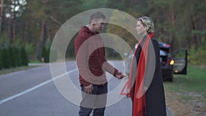 Young multi ethnic couple on the background of a broken vehicle standing on the side of the road. Handsome asian man