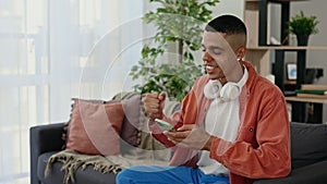 Young multi ethnic man reading good news on the smartphone at home. Satisfied african american male winning the lottery