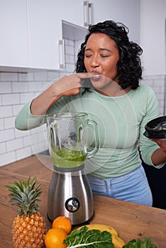 A young multi-ethnic woman tastes her freshly made green smoothie in the kitchen