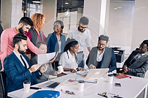 Young multi-ethnic work team exchanges ideas gathering around laptop computers