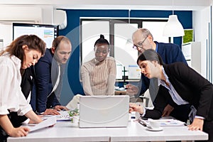 Young multicultural workers group talking, looking at laptop