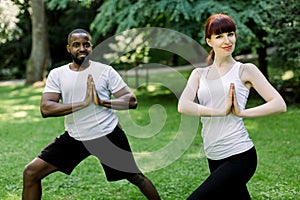 Young multiethnic couple, African man and Caucasian woman, doing yoga in nature outdoors, standing with hands together