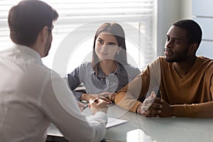 Young multiethnic couple consulting with male agent at office meeting