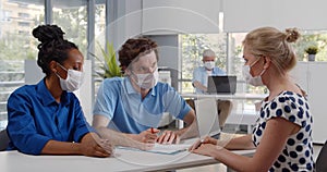 Young multiethnic couple in safety mask have meeting with realtor in office