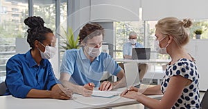 Young multiethnic couple in safety mask have meeting with realtor in office