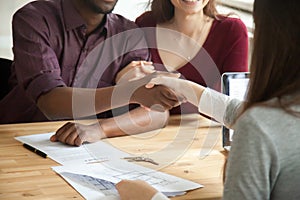 Young multiethnic couple shaking hands with real estate agent.