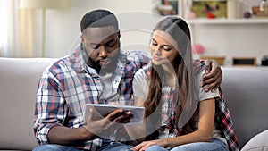 Young multiethnic couple using tablet at home, choosing goods online, shopping