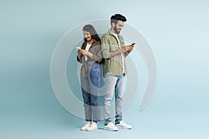 Young multiethnic man and woman hipsters using smartphones on blue