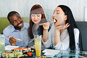 Young multiethnic people eating sushi rolls in Asian restaurant. Happy young friends enjoying leisure time and sushi at
