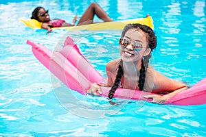 Young multiethnic women floating on inflatable mattresses in swimming pool