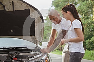 Young multiracial couple with a broken car in the middle of the road