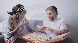 Young multiracial couple eating pizza from cardboardbox