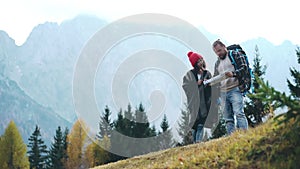 Young multiracial couple of hipsters walking with paper map and enjoy trekking or hiking. Caucasian man with backpack