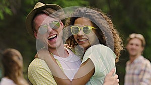 Young multiracial couple hugging, smiling and looking into camera at party