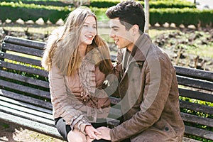 Young multiracial couple, male and female heterosexual students in love. A date in a city park on a wooden bench. Young brunette