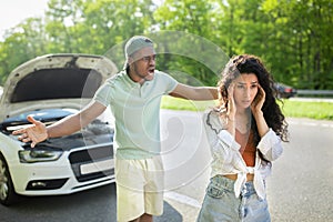 Young multiracial family having conflict on road near their broken car. African American guy shouting at his girlfriend