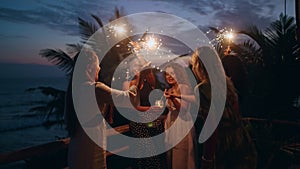 Young multiracial females having fun during celebration party in tropics with sparkling lights in their hands. Group of