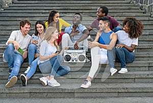 Young multiracial friends having fun listening music with vintage boombox stereo and using mobile smartphone